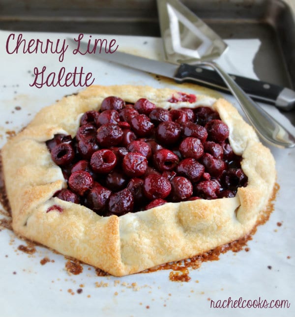 Baked cherry lime galette on parchment paper with serving utensils. Text overlay reads "Cherry Lime Galette. Rachelcooks.com"