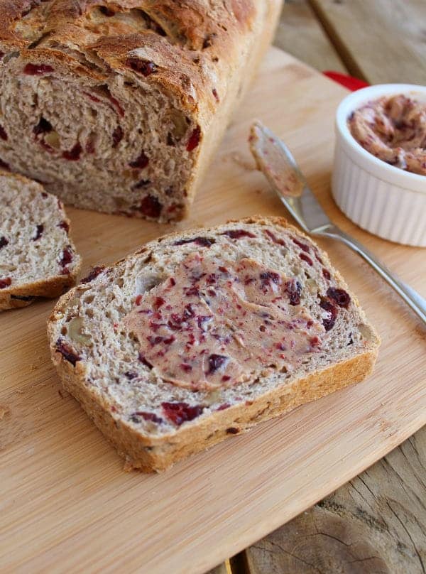Overhead of a slice of bread, spread with cranberry butter, with knife and crock of butter near by.