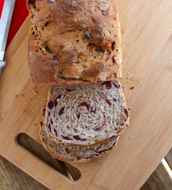 Partial overhead view of cranberry walnut loaf, partially sliced, on wooden cutting board.