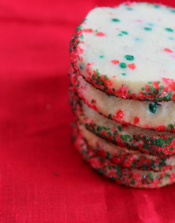 stacked shortbread cookies flecked with red and green sugar sprinkles on top of a red tablecloth