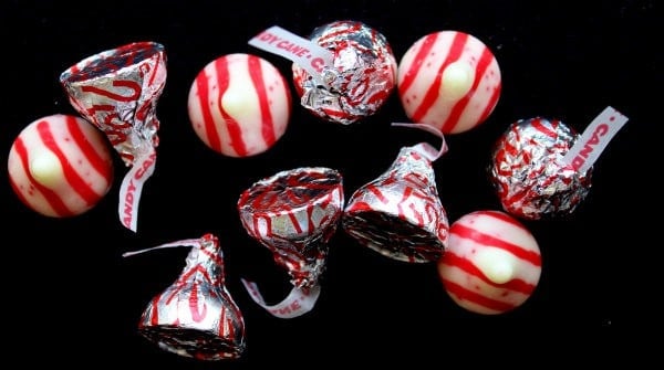 Several Candy Cane Kiss chocolates, both wrapped and unwrapped, on black background. 