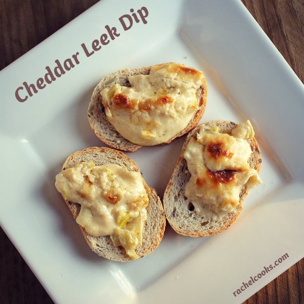 Overhead of three crostini with cheddar leek dip arranged on square white plate. Text overlay reads "cheddar leek dip, RachelCooks.com".