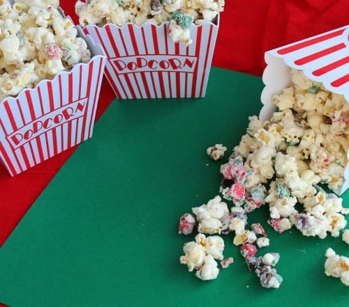 Peppermint popcorn spilling out of a popcorn container onto a green surface.