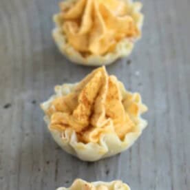A row of mini pumpkin pie tarts on a wooden table.