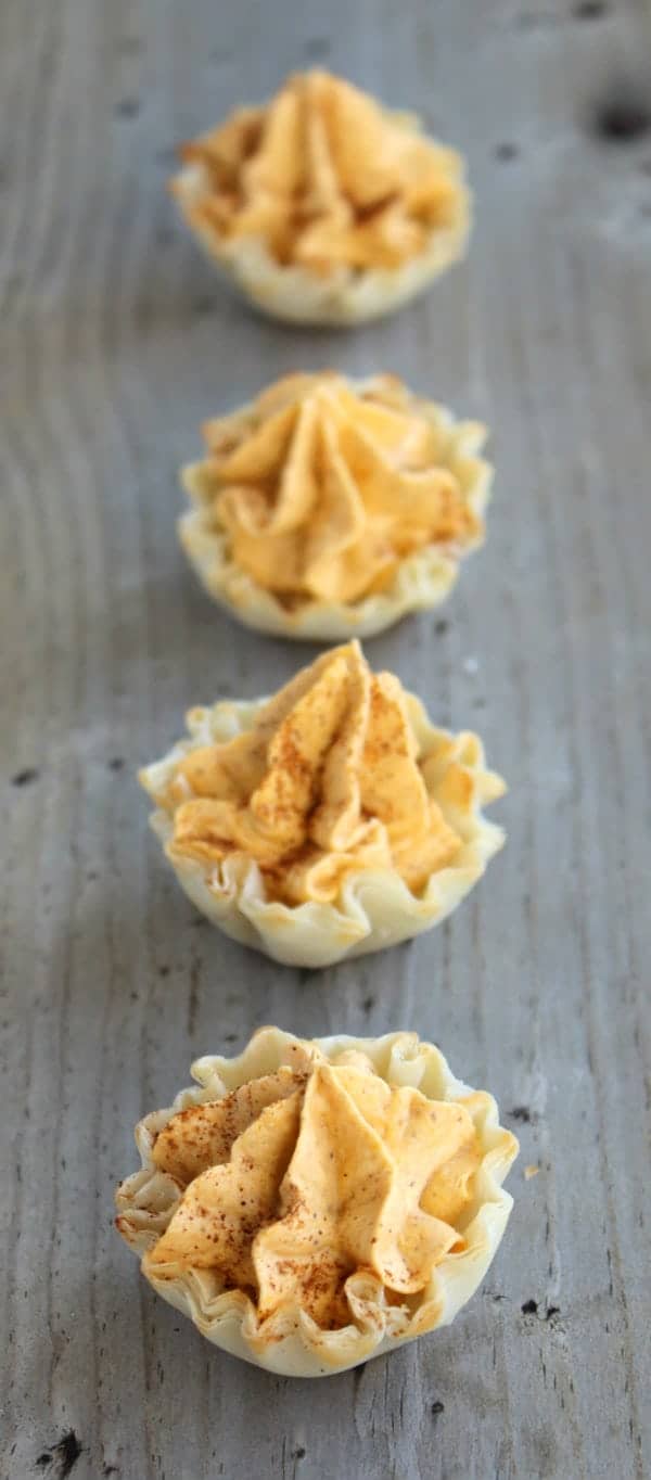 A row of mini pumpkin pie tarts on a wooden table.