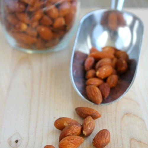 Almonds on a scoop and in a jar on a wooden surface.