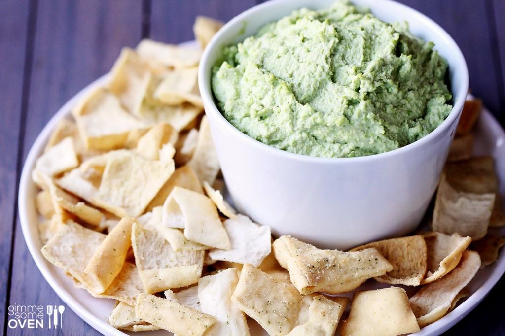 Close up view of edamame dip in bowl on plate with pita chips, with purple background.