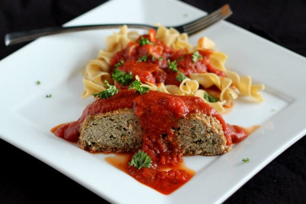 Serving of meatloaf on square white plate with fork. Served with marinara sauce and noodles.