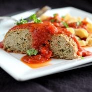 Serving of meatloaf on white plate with noodles and marinara sauce.