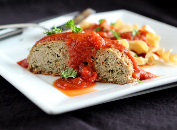 Front view of serving of meatloaf on white plate with noodles and sauce.