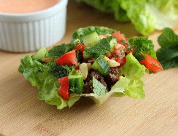 Front view of lamb lettuce wrap with small white bowl of sauce in background.