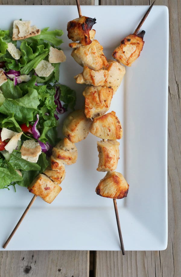 Partial overhead of skewers and salad on white plate.