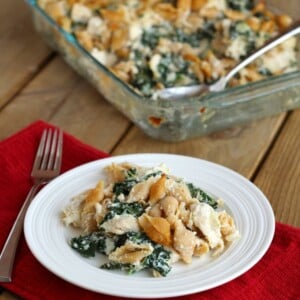 Chicken and kale casserole on white plate, with clear glass casserole pan in background.
