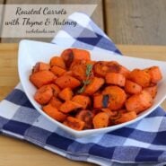 Roasted carrots in white bowl on blue checked folded napkin.