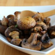 Close up of white dish containing roasted mushrooms and wooden spoon.