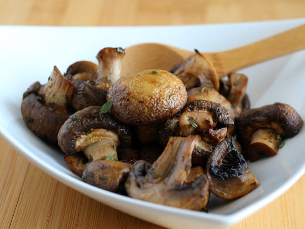 Close up front view of roasted mushrooms in white dish.