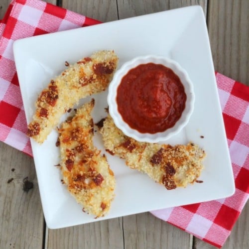 Overhead view of plate containing chicken tenders, on a red checked napkin.