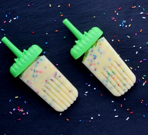 Overhead of two popsicles on black background with funfetti sprinkled around them.