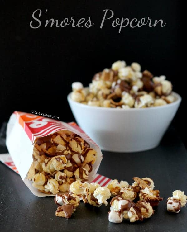 Front view of a popcorn bag tipped over with s'mores popcorn spilling out. White bowl of popcorn in background. Text overlay reads, "S'mores popcorn".