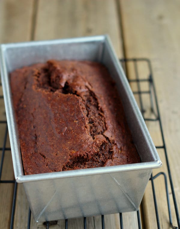 Baked bread in metal loaf tin on cooling rack.