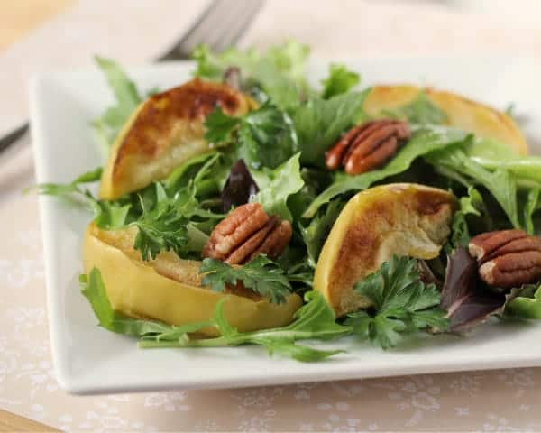 Front view of salad with broiled apples on square white plate.