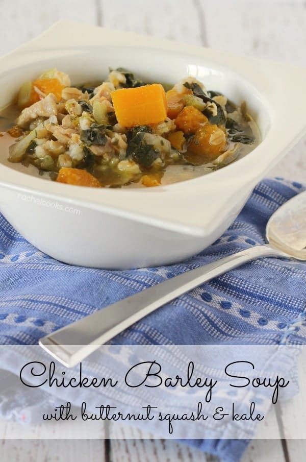 Front view of chicken barley soup in white bowl, with spoon along side, on a blue patterned cloth. Text overlay reads "Chicken barley soup with butternut squash & kale."