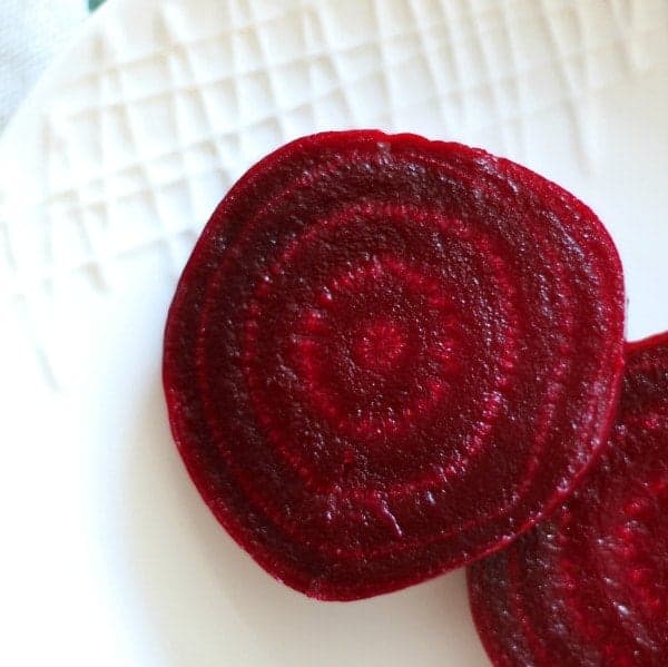 Close up top view of sliced beets on white plate.