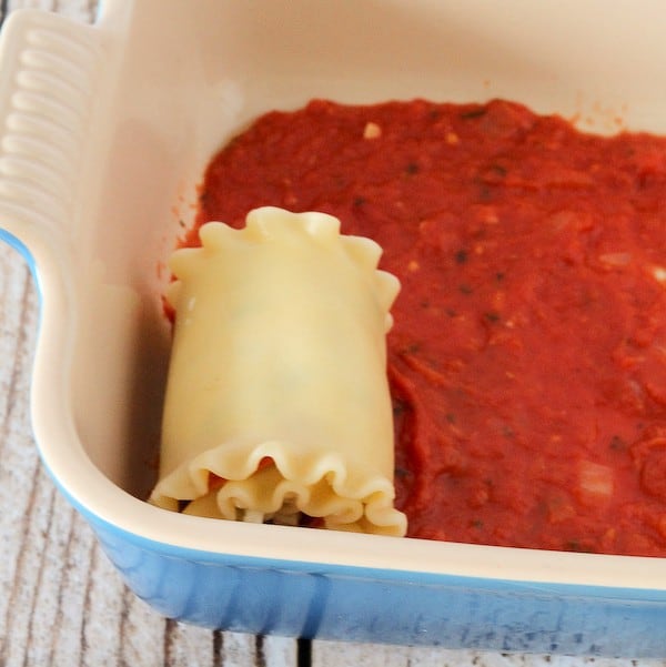 A cooked, rolled up lasagna noodle in a pan with tomato sauce in the bottom of it.
