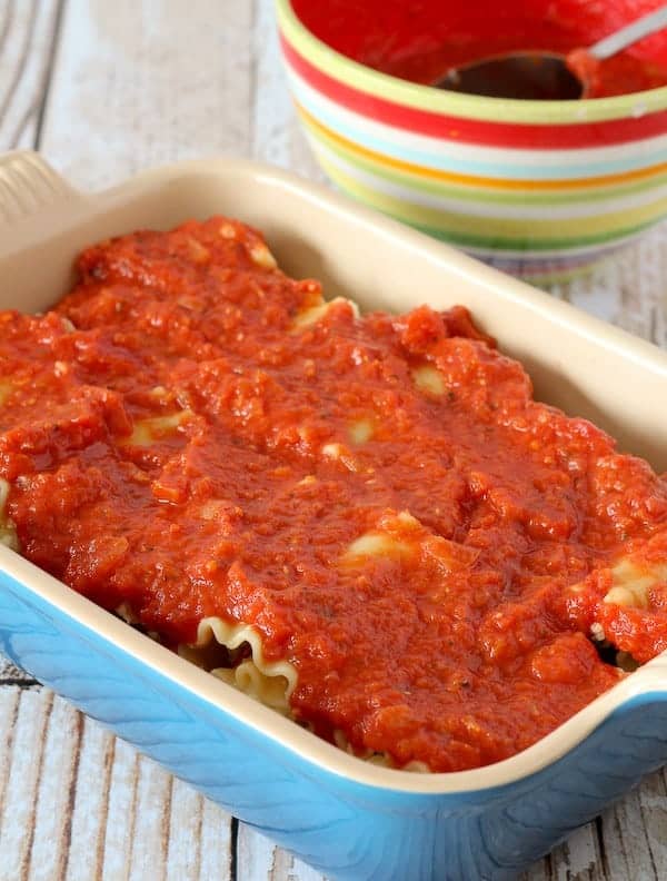 A blue baking dish filled with lasagna rolls covered in tomato sauce.