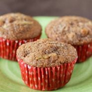 Three apple bran muffins with red liners on a green plastic plate.