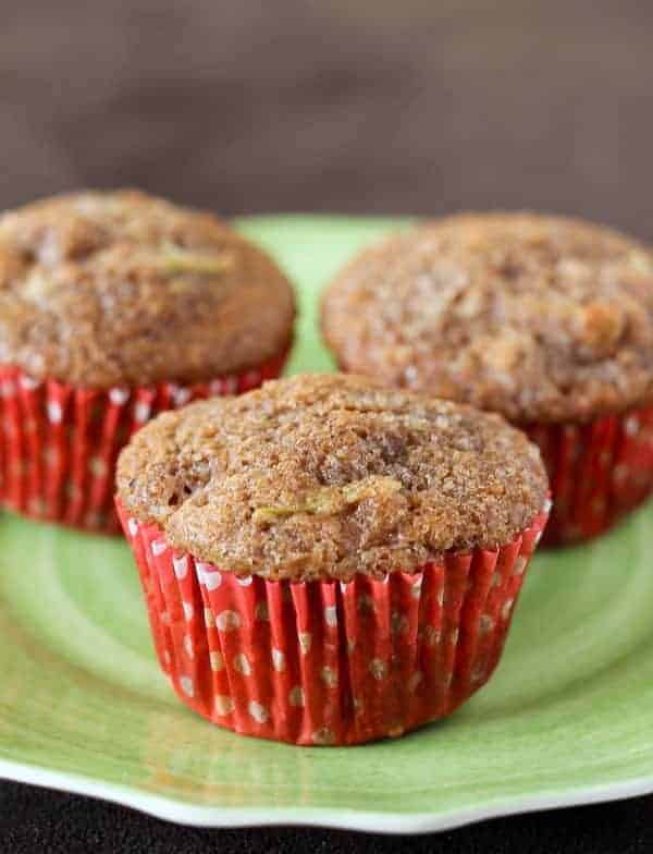 Three apple muffins on a green plate with red muffin liners.