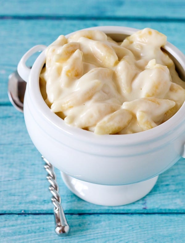 Shell shape mac and cheese in a white bowl against a blue background.
