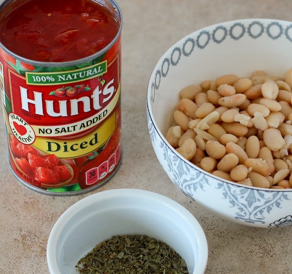 Diced tomatoes in can, bowl containing white beans, bowl containing dried herbs.