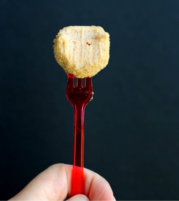 Partial image of hand holding red plastic fork inserted into cheesecake ball, with bite taken.