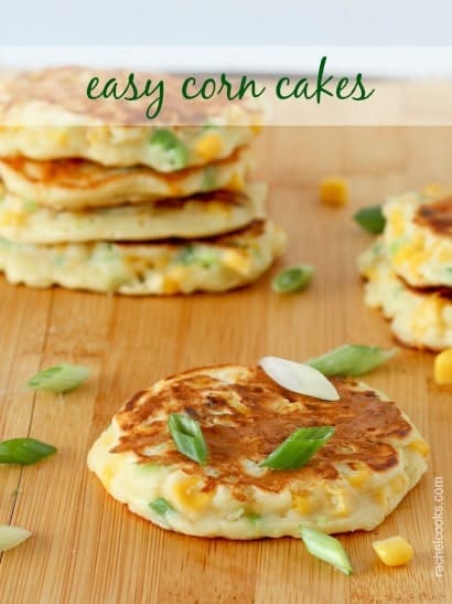 Several corn cakes on wooden cutting board, with sliced green onions and corn kernels scattered between them. Text overlay reads "easy corn cakes."