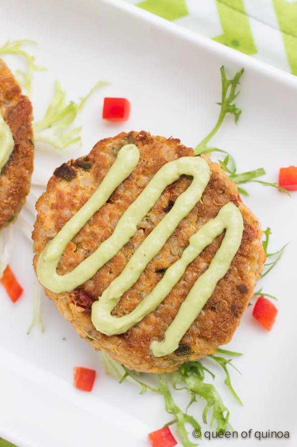 Quinoa crab cake on white plate garnished with creamy light green sauce drizzled on decoratively.