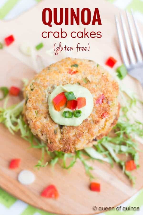 Crab cake on bamboo cutting board, garnished with light green sauce, chopped red bell pepper, sliced green onion, and shredded lettuce. Text overlay reads "Quinoa crab cakes (gluten-free).