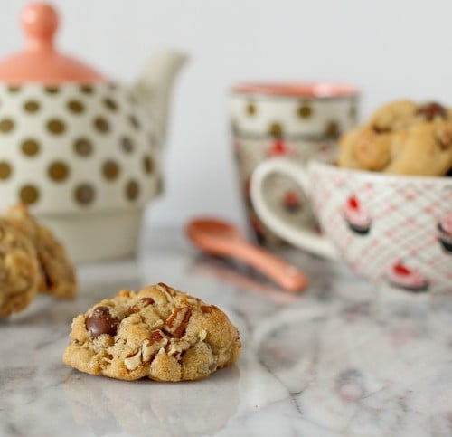 Arrangement of cookies, teapot, spoon, cups, on white marble surface.