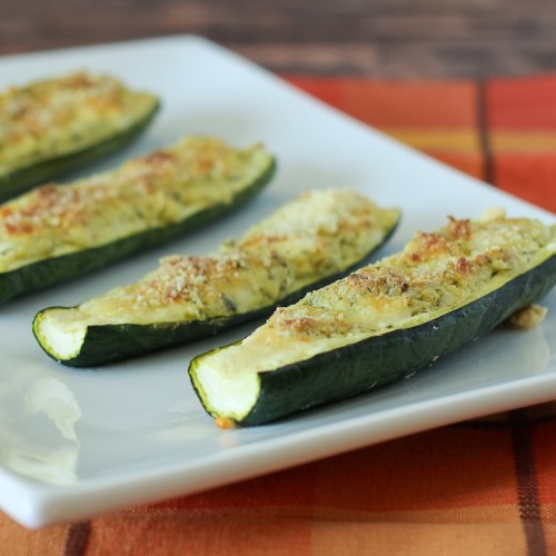 Partial image of white platter containing 4 cheese stuffed zucchini, on orange plaid cloth.