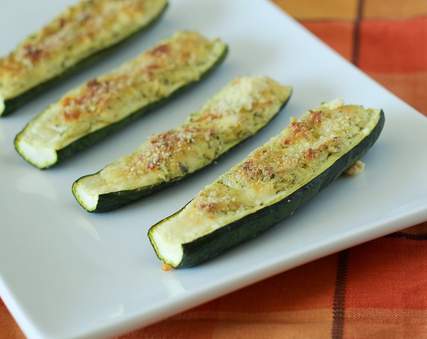 Partial image of white platter containing 4 cheese stuffed zucchini, on orange plaid cloth.