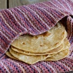 Closeup side view of 4 tortillas, partially wrapped in woven cloth.