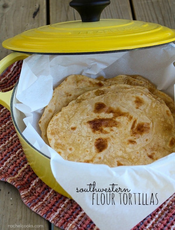 Overhead view of a stack of tortillas in yellow Dutch oven with lid ajar, lined with parchment paper. Text overlay reads Southwestern flour tortillas.