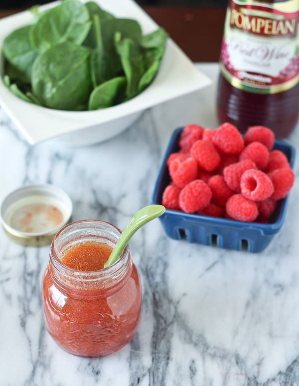 Overhead front image of dressing, raspberries, spinach, and vinegar.