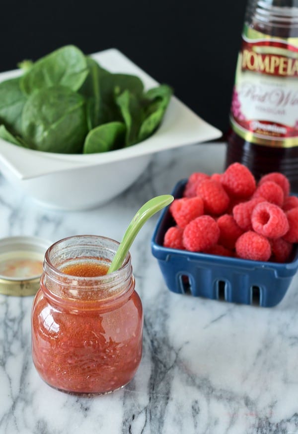 Overhead front view showing open jar of dressing, a basket of raspberries, a bowl of spinach leaves, and a bottle of Pompeian Red Wine Vinegar.