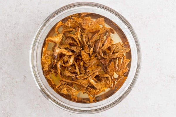 Dried chanterelle mushrooms soaking in a glass bowl of hot water.