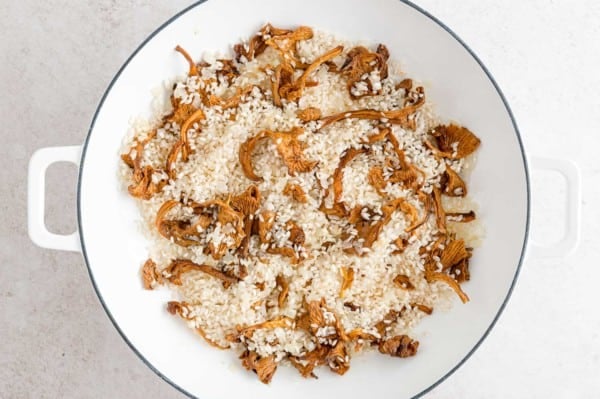 Risotto rice added to a skillet with chanterelle mushrooms.