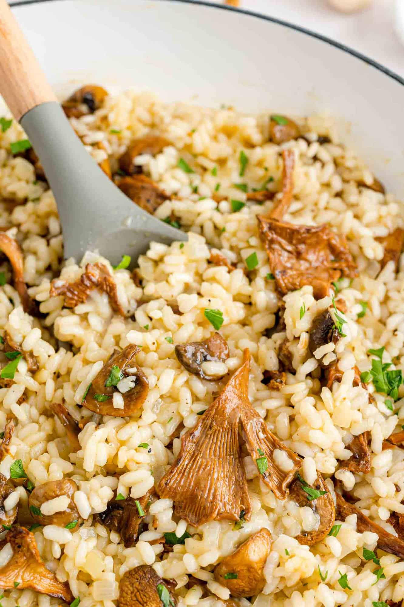 A large serving spoon stuck into a pot of mushroom risotto.