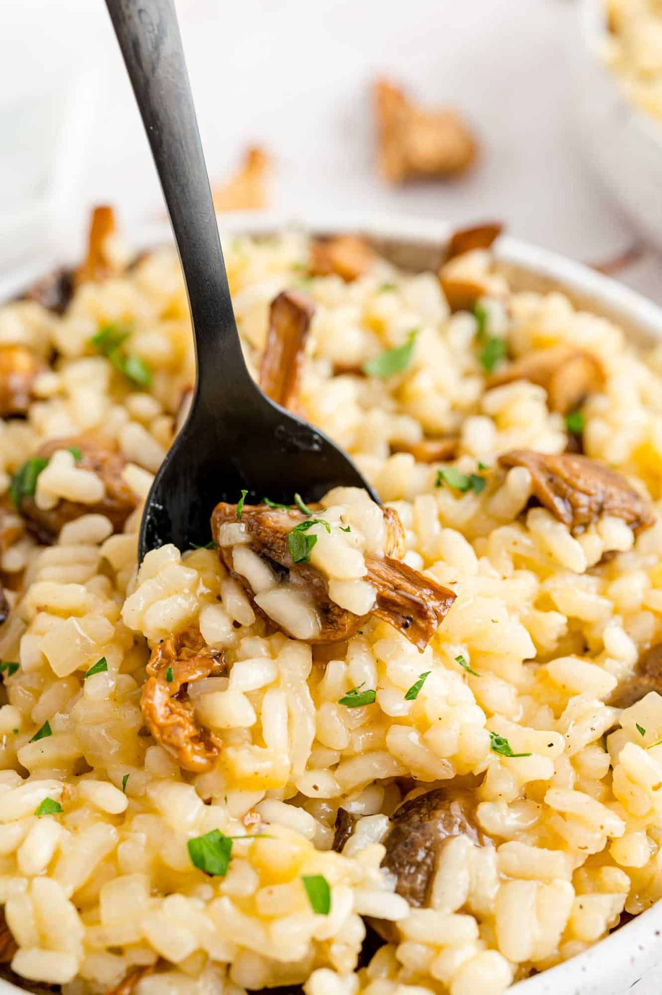 Rich and creamy mushroom risotto is a comforting dish loaded with garlicky roasted mushrooms and herbs, perfect for any night of the week. A spoon stuck into a bowl of mushroom risotto.
