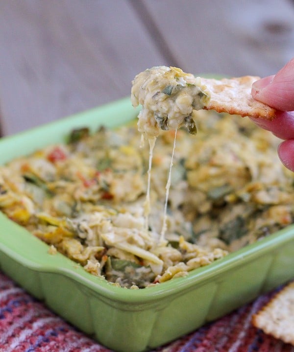 Partial image of dip in casserole dish with fingers dipping a cracker into the dip.