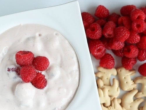 Partial image of dip in square white bowl with raspberries and animal crackers alongside.